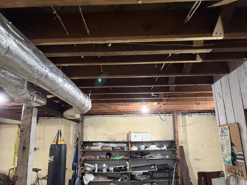 Bare wood floor joists and ductwork with no insulation